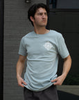 Man wearing a light blue t-shirt with a white geometric design against a brick wall.