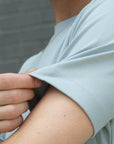 Person wearing a light blue shirt with sleeves rolled up, against a gray background