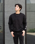 Man wearing a black outfit standing in front of a modern building.