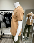 Mannequin wearing a tan t-shirt with a white logo, standing in front of a mirror reflecting the same outfit.