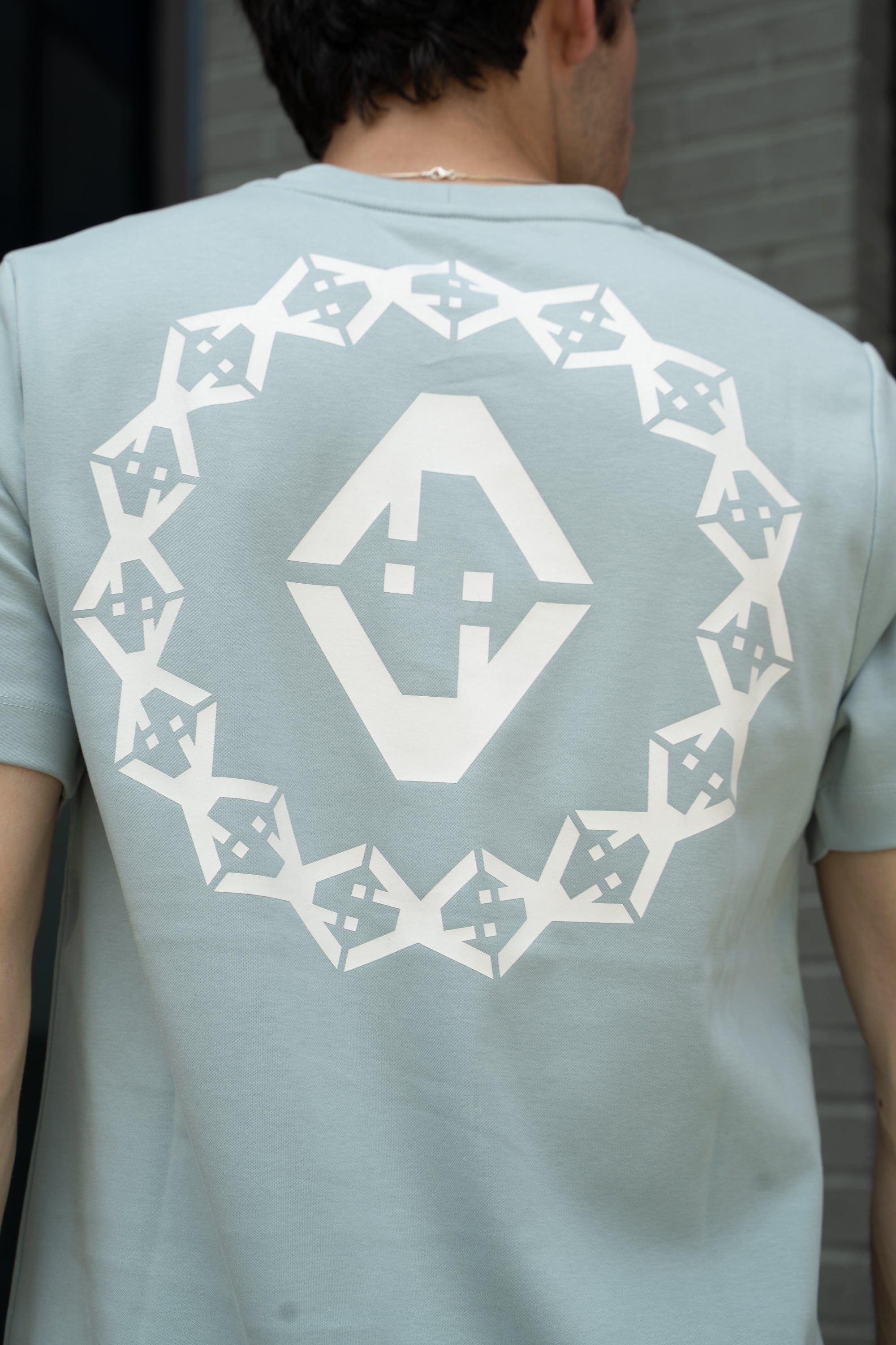 Light blue t-shirt with white geometric pattern on the back, worn by a person.