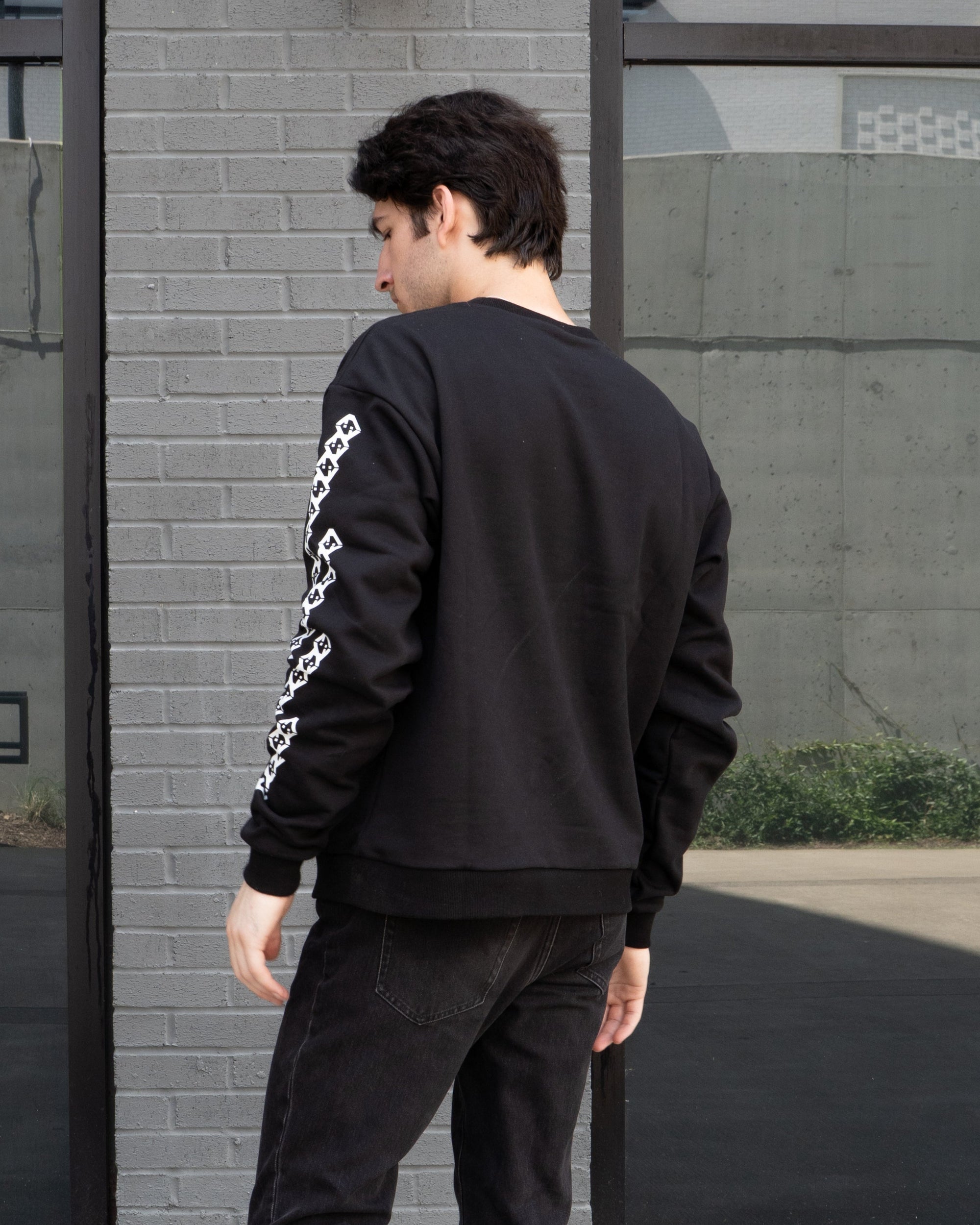 Person wearing a black sweatshirt and pants standing against a gray wall.