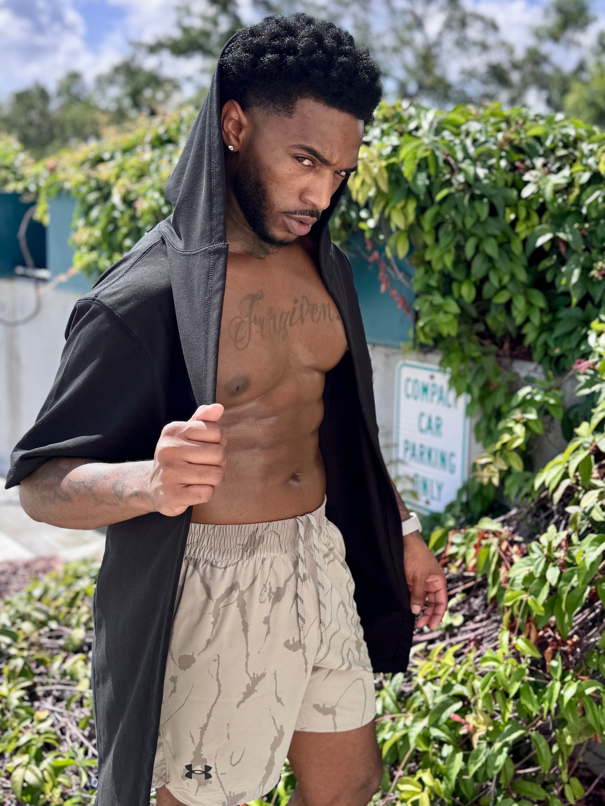 Man with a shirt over his shoulder standing outdoors with greenery in the background