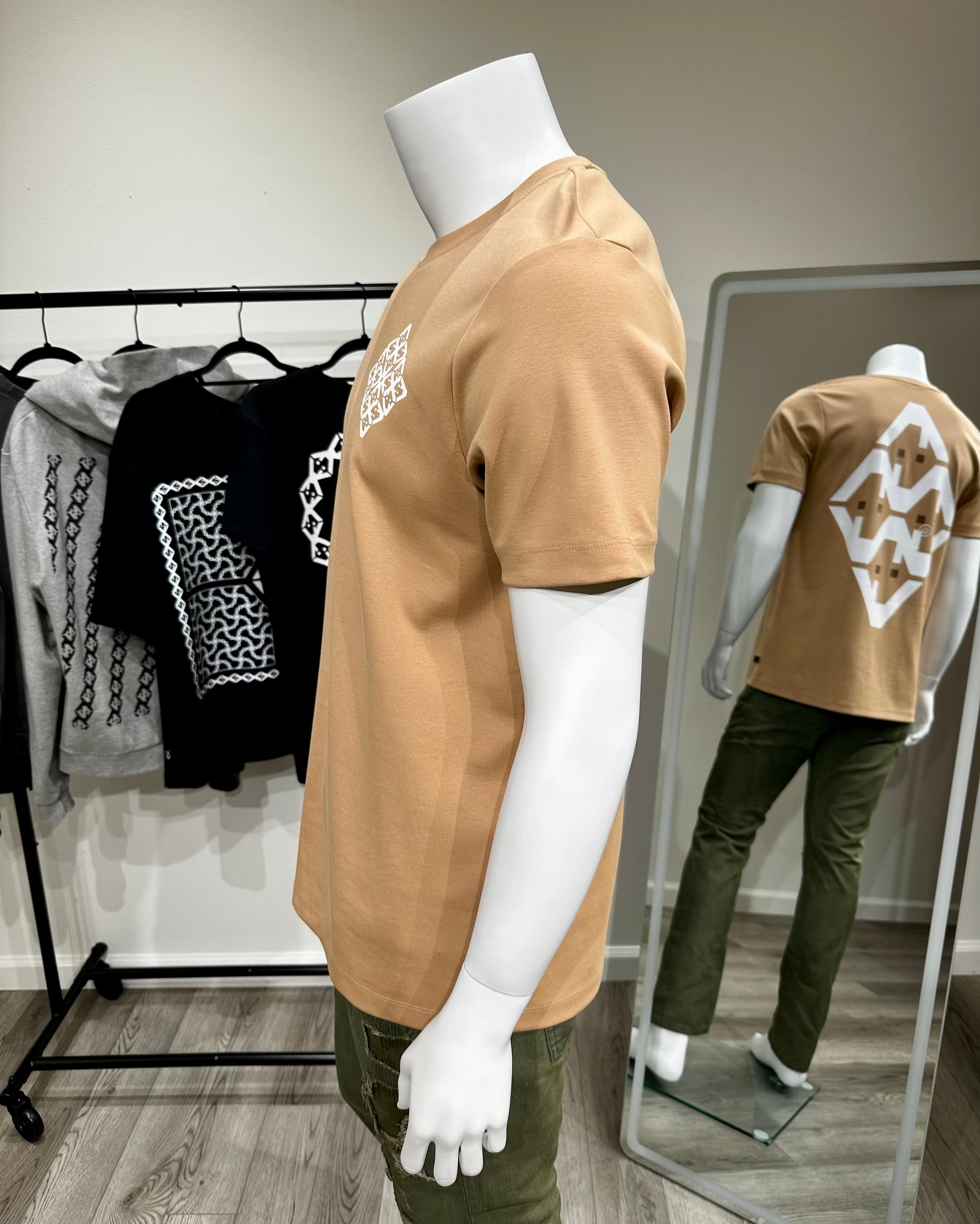Mannequin wearing a tan t-shirt with a white logo, standing in front of a mirror reflecting the same outfit.